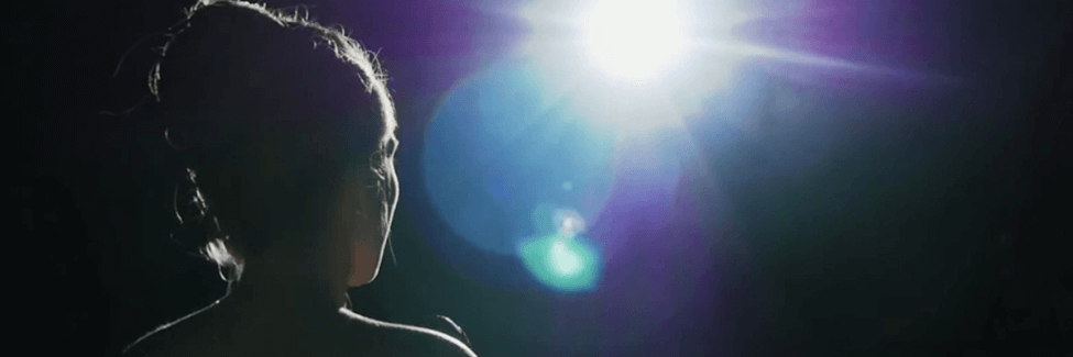 An almost silhouette of a women from behind in front of a stage in the spotlight.